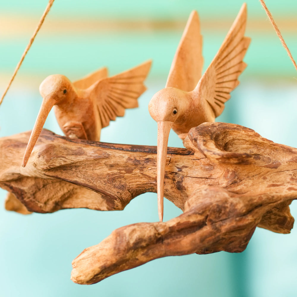 Wooden hummingbird figurines on a branch against a blurred background